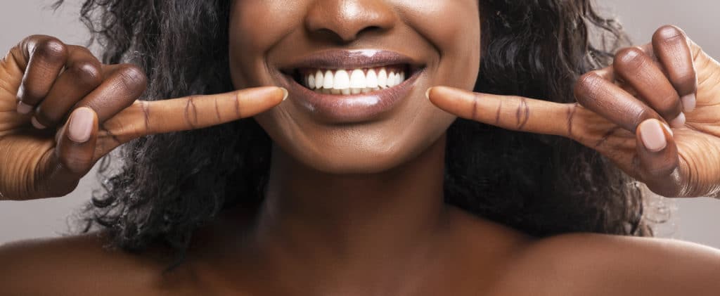 Orthodontic concept. Unrecognizable african american girl pointing at her healthy white teeth and widely smiling, panorama