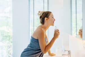 woman looking at mirror and brushing teeth with water floss.