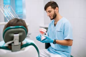 Male dentist shows dentures with a bracket in her hands to the patient. False teeth in the hands