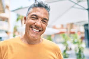 Mature man gives a big smile while at an outdoor market, confident with healthy gums and teeth.