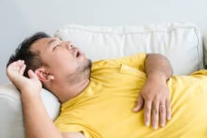 Asian dad falls asleep and snores loudly on the couch.