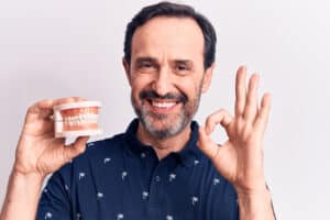 Man in his 50s holds up dentures ahead of receiving new teeth.